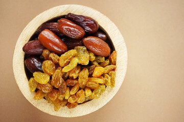 Dried dates and raisins in a wooden plate on a light background