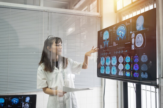 Female doctor presenting x-ray film brain human of patient on digital monitor showing MRI, CT scans brain images. Doctor Scientist checking examining viral infection on monitor