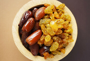 Dried dates and raisins in a wooden plate on a beige-brown background