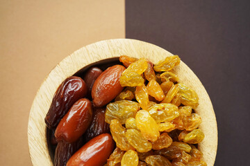 Dried dates and raisins in a wooden plate on a beige-brown background