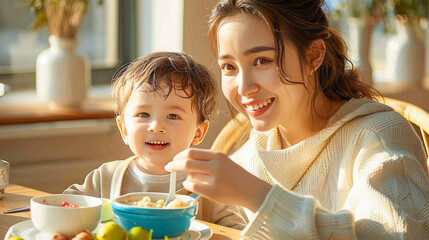 Young mother smiles feeding little toddler son with milk cereal from spoon. Babysitter spends time with baby feeding with spoon of delicious food for kids. Family spends time. Children nutrition