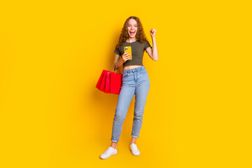 Photo of cheerful lovely girl dressed stylish clothes hold packages seasonal sale low price fist yes isolated on yellow color background