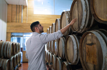 Professional man winemaker working and inspecting wine quality in wine cellar with wooden barrel in wine factory. Winery manufacturing industry, Alcohol and winemaking fermentation process.