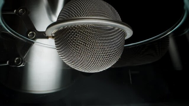 Making tea, a metal strainer inside which tea leaves are poured with boiling water. Macro view from inside the glass.