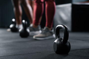 Person stands by grey kettlebell on gym floor by wood flooring