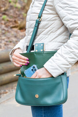 woman takes out smartphone from handbag outdoors, vertical photo