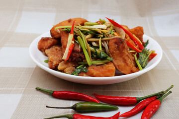 Crispy fried fish, stir-fried celery and spring onions Sliced ​​red peppers are placed on top. in a white porcelain plate On the table with fresh chilies in front

