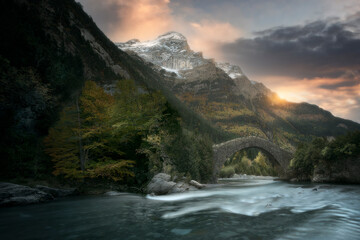 Dawn in the Bujaruelo valley, in the Aragonese Pyrenees, with the sun rising between the mountains and in front of the Romanesque bridge and the Ara river