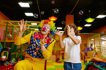 Little preschool boy and clown playing with soap bubbles