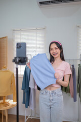 Young Asian Female online seller is using smartphone live on internet introduce new fashion cloth...