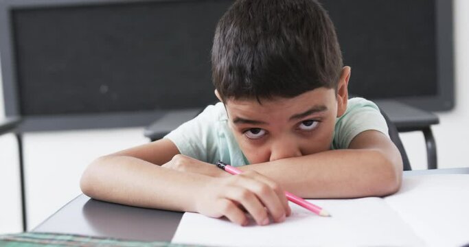 In a school classroom, a young biracial boy rests his head on his arms