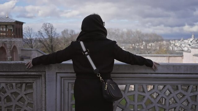 A woman gazes across the historic skyline of istanbul from topkapi palace under a cloudy sky.