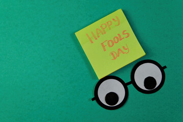 Happy Fools day text on sticky notes with funny faces on green background