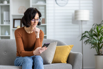 Obraz premium Woman in orange sweater using smartphone on couch