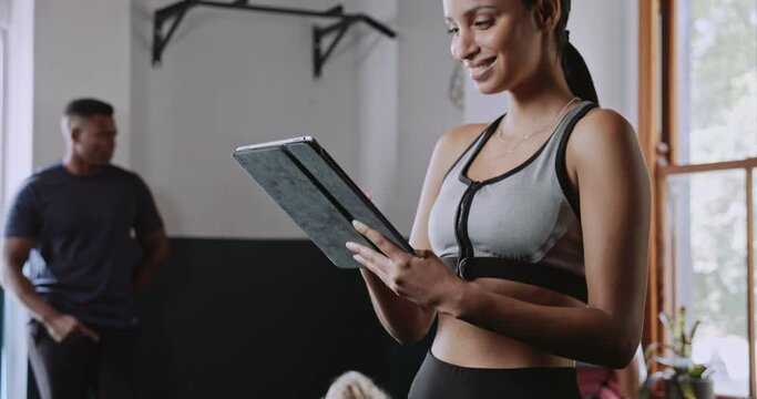 Young multiethnic woman uses tablet in fitness studio before training session 