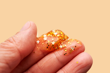 Cosmetic gel with glitter on women's fingers on a beige background.