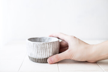 A woman's hand holds an empty white ceramic handmade coffee cup. A place to copy. Front view.