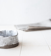 An empty ceramic bowl made of gray clay on a white table against a background of a linen napkin. A place for the text.