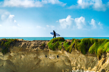 Surfer walked toward the cliff end at the iconic West Cliff Drive surf spot in Santa Cruz, CA.