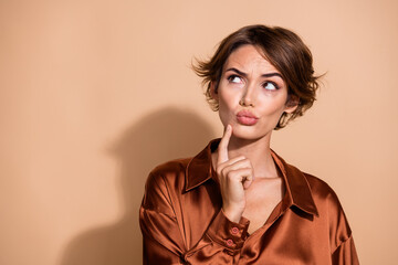 Photo of uncertain suspicious lady dressed silky shirt finger chin looking empty space isolated beige color background