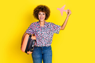 Photo of excited positive woman wear animal print shirt holding luggage rising plane card isolated yellow color background