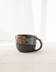 An empty handmade ceramic coffee cup with streaks of glossy glaze on a light background. Front view.