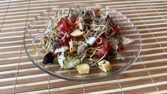 Salad of fresh vegetables and microgreens. Tomatoes, onions, apples, a mound of sprouted mung beans, sesame seeds, flax and cheese cubes on a transparent plate. Chef's hand puts dish on the table