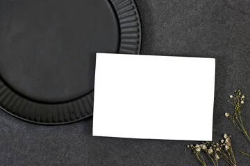 Wedding invitation card mockup above black ceramic plate with gypsophila on gray background. Blank...