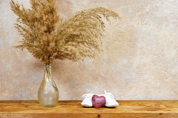 Gender neutral baby shoes with  pink glitter heart and reeds vase on wood table