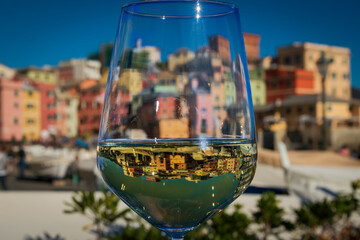A glass of Vermentino Wine in front of Boccadasse, the pitoresque fishermen village nearby Genoa.  - obrazy, fototapety, plakaty