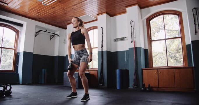 Woman lifting kettlebell over head in gym with flooring