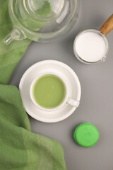 Fototapeta na wymiar healthy matcha green tea in a white cup. next to it is a transparent teapot, green macaroons and a vessel of milk. view from above