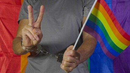 The man holds the rainbow flag and with the other hand makes the victory sign at the camera despite...