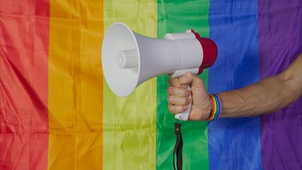 Hand holds megaphone in front of rainbow flag. LGBT rights concept