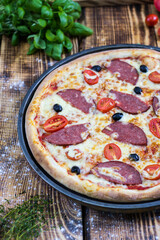 A rustic wooden table with a whole homemade pizza and the ingredients from which it is made at the back.