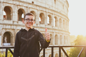 Smiling happy tourist  boy with   eyeglasses  enjoy Colosseum in the old city center of Rome, Italy. Concept  family travel trip.