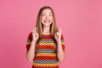 Photo of positive cute girl closed eyes beaming smile crossed fingers empty space isolated on pink...