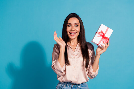Photo of ecstatic crazy woman with straight hairdo dressed silk shirt holding present box in palm isolated on blue color background