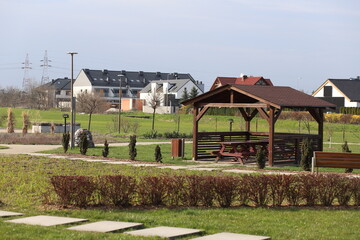 Fototapeta na wymiar Park area in front of the new building. Elite housing complex. Haze on the horizon. Sunny weather and haze among the houses. Wooden gazebos for relaxation.
