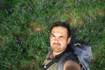 Naklejka na ściany i meble A man with a backpack smiles while taking a selfie in a field of purple flowers