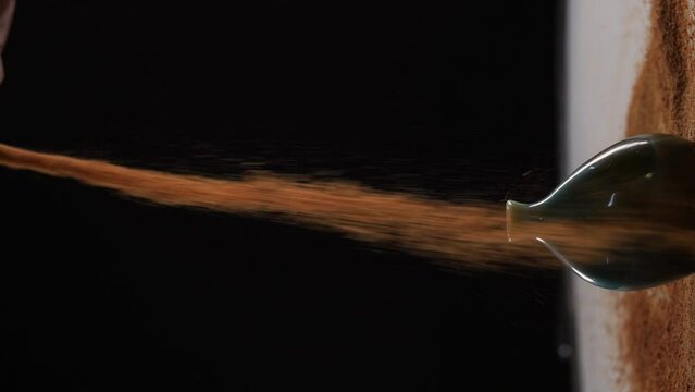 Filling a small vessel with cocoa powder against black background