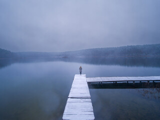 Woman is Standing on the Edge of Wooden Pier, Jetty, Dock at Peaceful Snowy Winter Lake, Silhouette