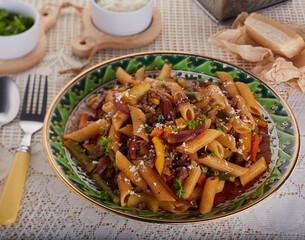 Pasta dish with minced beef and mixed vegetables in a rich sauce and garnished with herbs and grated  cheese.