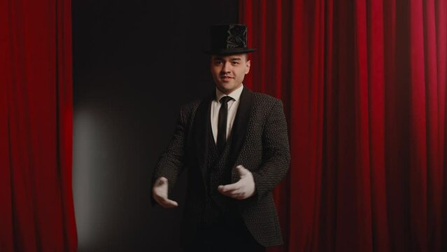 Smiling fashionable showman or illusionist in tailcoat and top hat on stage