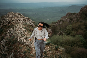 Naklejka na ściany i meble Woman happy tourist hiking up runs from top of mountain enjoying nature. Landscape in cloudy gloomy windy weather at summer. Excited female in joy, enjoying travel. Freedom concept