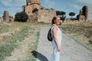 Happy senior traveling mature woman backpacker tourist outdoors in ancient Europe fortress ruins. Retired people summer holiday vacation, active lifestyle concept. Jvari Monastery, Mtskheta, Georgia