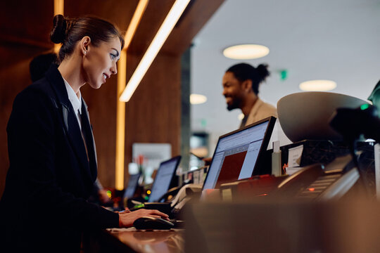 Smiling hotel manager working on computer at reception desk.