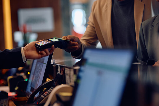 Close up of African American man using credit card while paying at hotel reception desk.