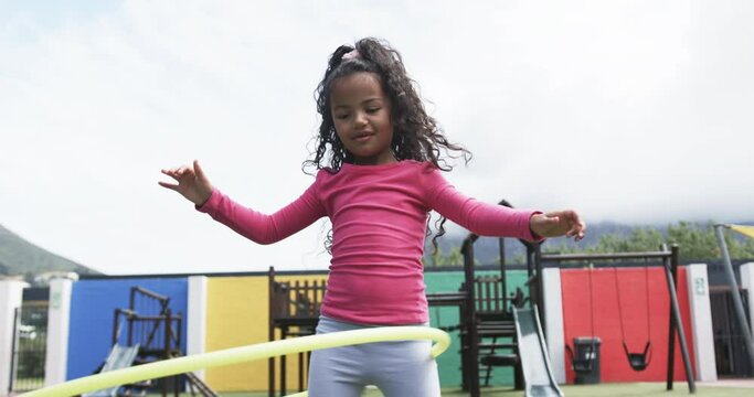 In a school playground, a young African American girl is hula hooping