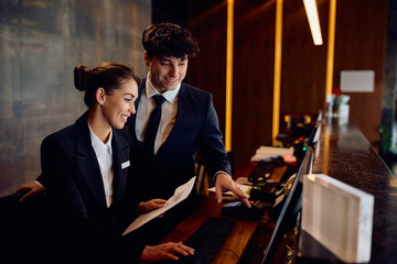 Happy receptionists cooperating while working on  computer at hotel front desk.